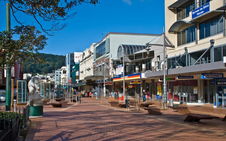 Evening view of Wellington's Courtney Place, featuring bustling nightlife with people enjoying outdoor seating at cafes and bars, illuminated by warm streetlights under a cloudy sky